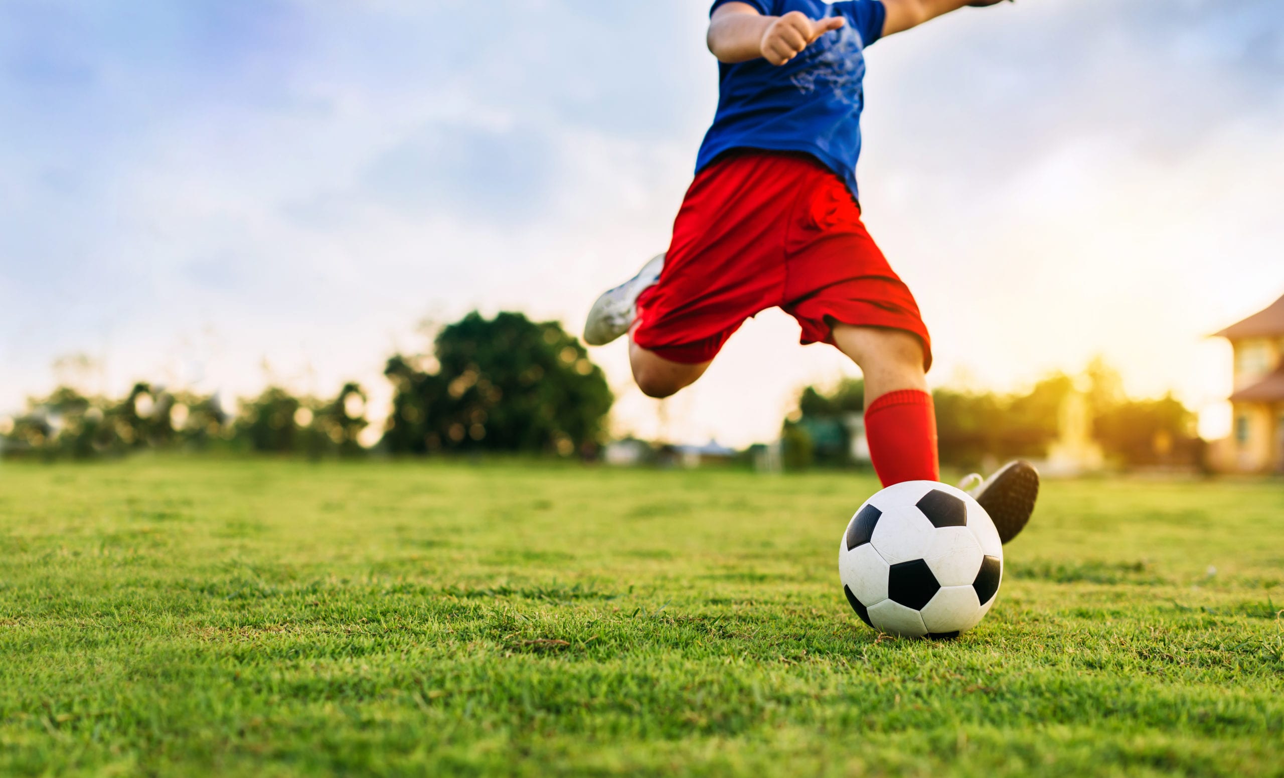 An action sport picture of a group of kids playing soccer football for exercise in community rural area under the sunset.