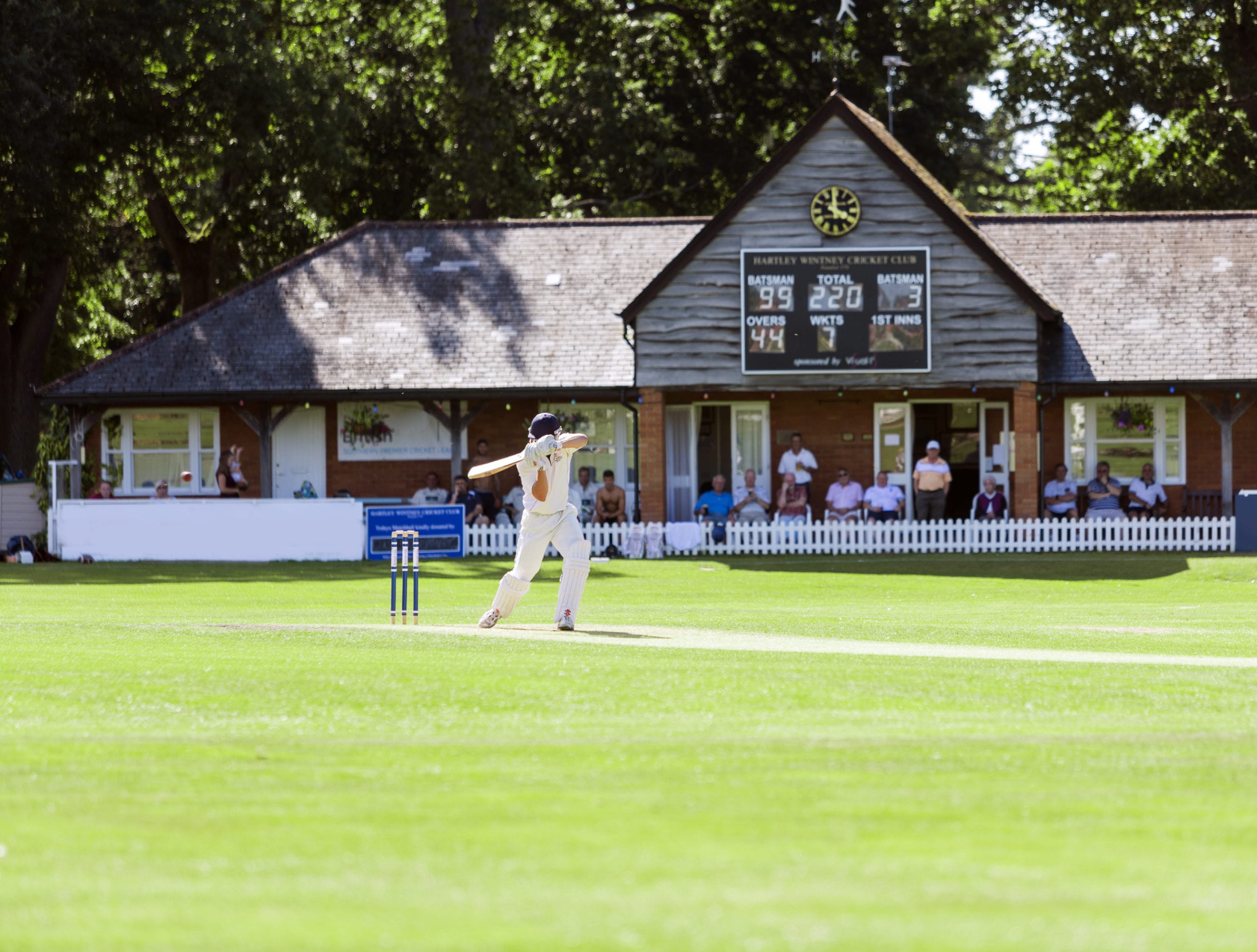 cricket player in all white batting ball on green field